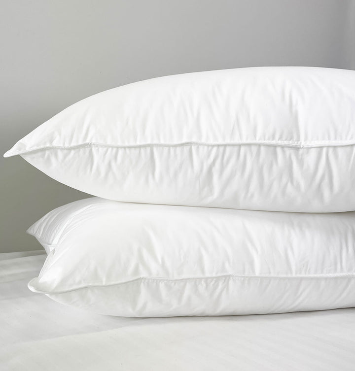 Two down alternative hotel pillows sitting on top of each other on a white bed